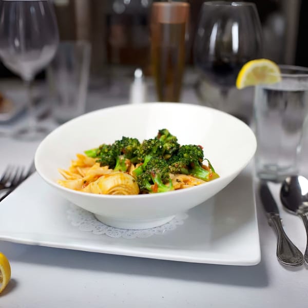 Italian farfalle pasta with broccoli and artichoke hearts in a white bowl on a set table.