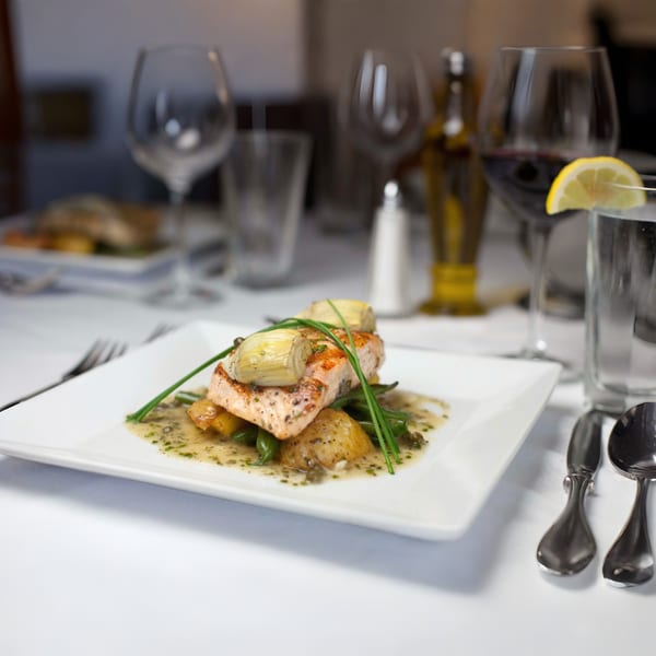 Italian salmon dish with artichokes, green beans, and potatoes on a white plate.