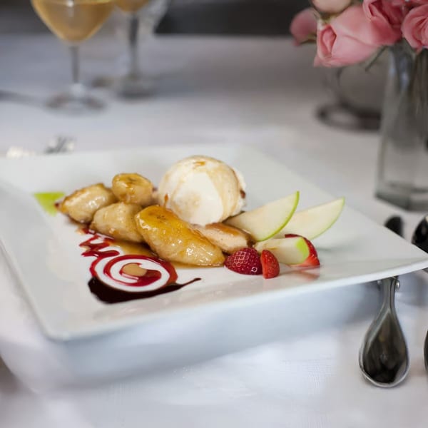Caramelized bananas with vanilla ice cream, strawberries, and apple slices on a white plate.