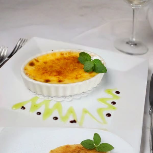 Crème brûlée with a mint garnish, drizzled with green and chocolate sauces on a white plate.