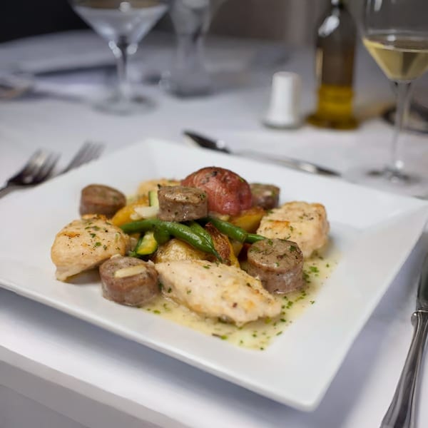 Italian chicken and sausage with roasted potatoes and green beans on a white plate.